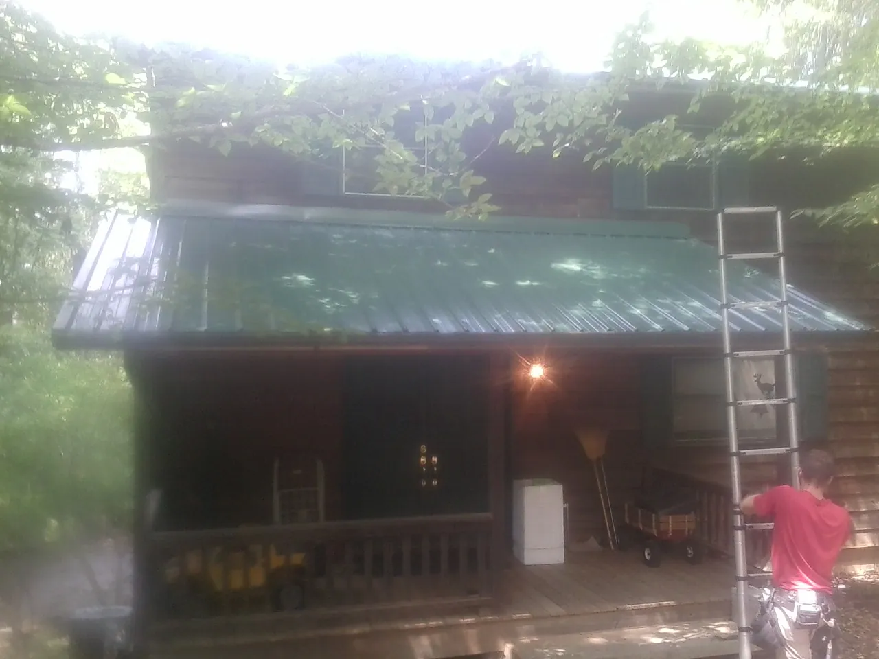 Worker on a ladder at the green porch roof of a wooded cabin in Taylorsville