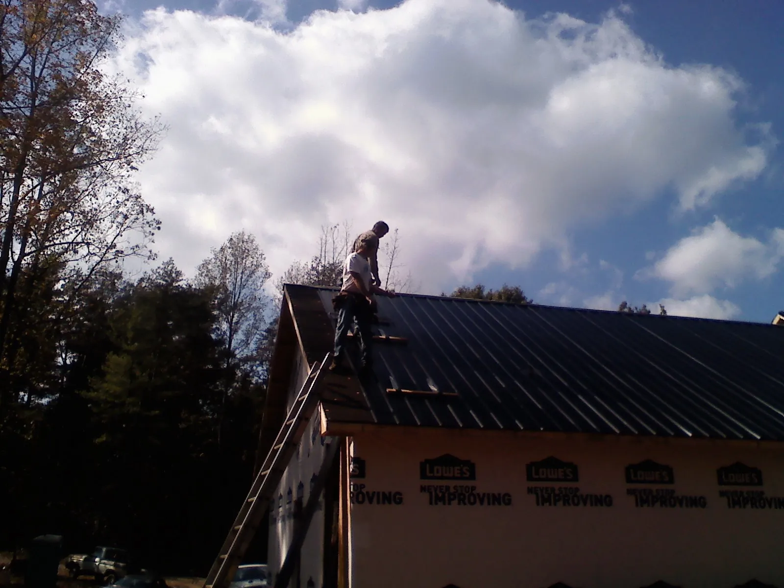 Roofer fastening dark metal panels high against a cloudy sky, from a Roof Inspection job in Taylorsville